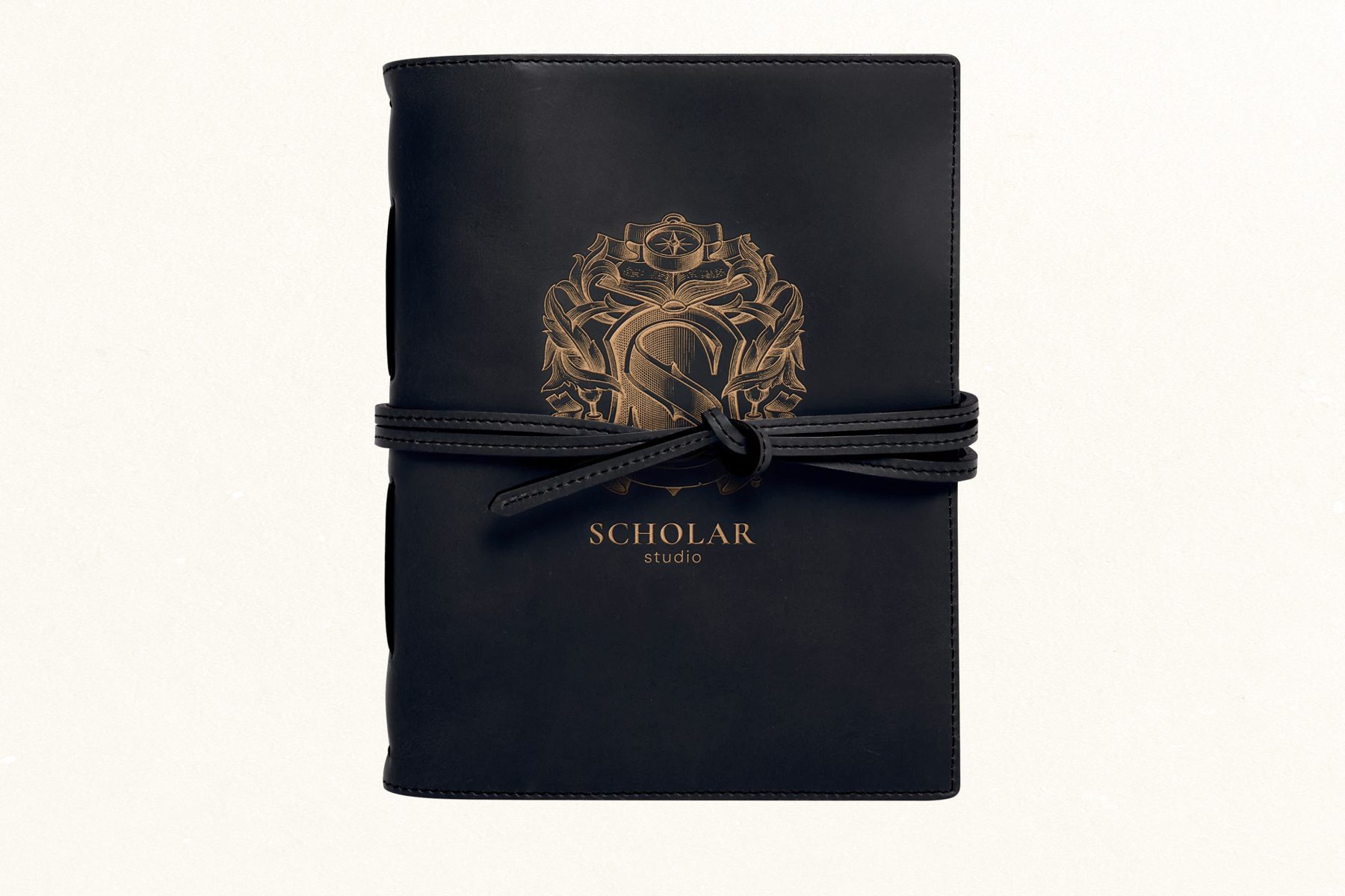 A navy leather field journal tied with a leather cord, stamped with the gold Scholar Studio crest